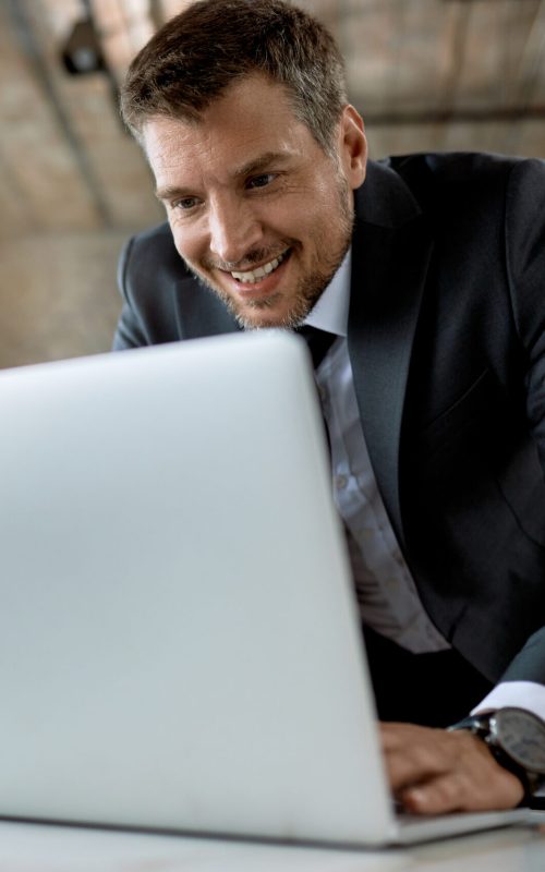 Happy entrepreneur typing an e-mail while working on laptop in the office.